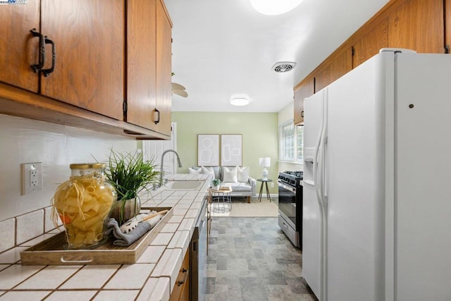 kitchen with white refrigerator with ice dispenser, stainless steel range with gas stovetop, tile counters, and sink