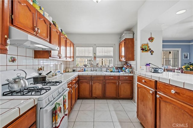 kitchen featuring sink, tile countertops, white gas range oven, and backsplash