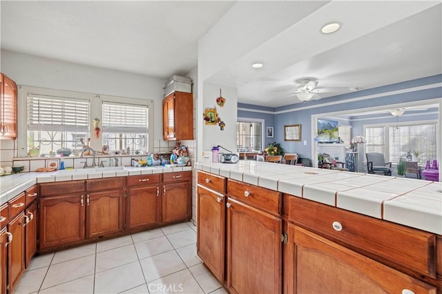 kitchen with light tile patterned flooring, a healthy amount of sunlight, tile countertops, and ceiling fan