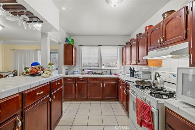 kitchen with light tile patterned floors, sink, backsplash, tile counters, and white gas range