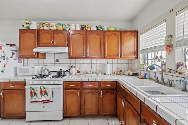 kitchen featuring sink, light tile patterned floors, tile counters, white appliances, and decorative backsplash