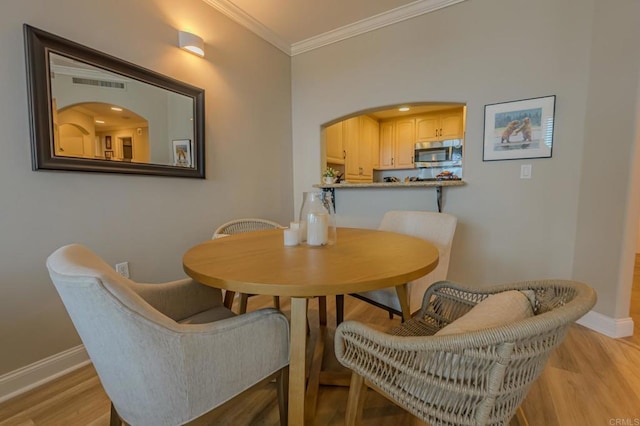 dining room featuring arched walkways, crown molding, light wood finished floors, visible vents, and baseboards