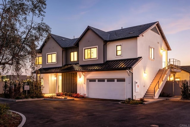 view of front facade with aphalt driveway, metal roof, an attached garage, a standing seam roof, and stairs