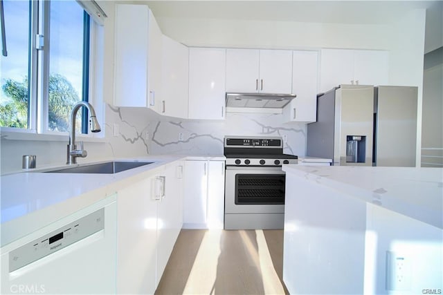 kitchen featuring sink, appliances with stainless steel finishes, white cabinetry, tasteful backsplash, and light stone countertops