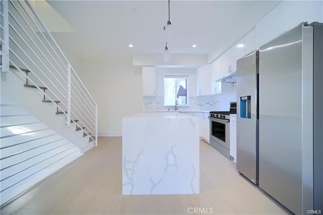 kitchen featuring appliances with stainless steel finishes, decorative light fixtures, white cabinetry, backsplash, and light stone counters