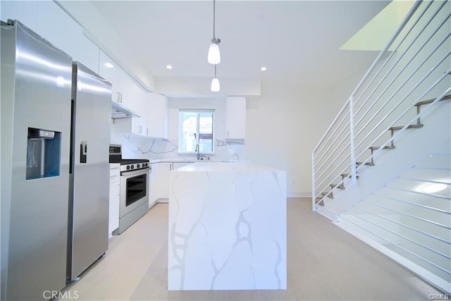 kitchen with appliances with stainless steel finishes, white cabinetry, hanging light fixtures, light stone counters, and decorative backsplash