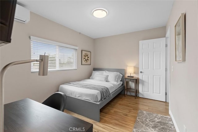 bedroom featuring baseboards, an AC wall unit, and light wood-style floors