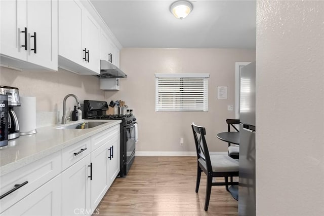 kitchen featuring black range with gas cooktop, under cabinet range hood, a sink, white cabinetry, and freestanding refrigerator