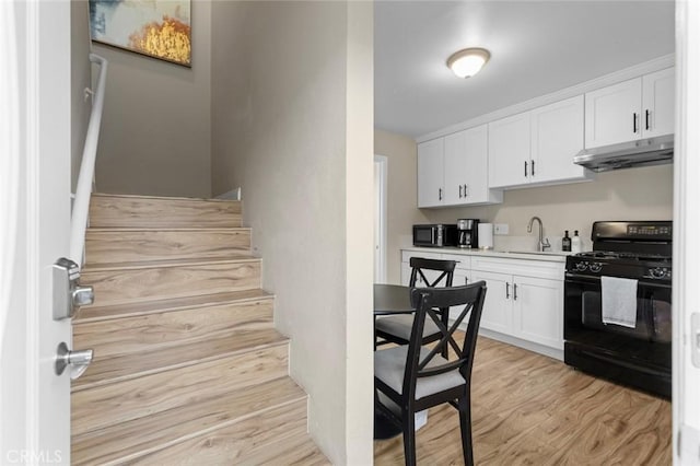 kitchen featuring black gas range oven, light countertops, light wood-type flooring, under cabinet range hood, and white cabinetry