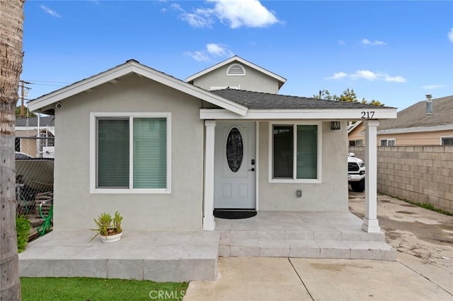 bungalow with a shingled roof, fence, and stucco siding