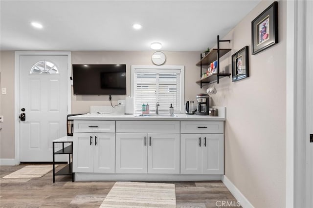 kitchen with a sink, baseboards, white cabinets, and light countertops