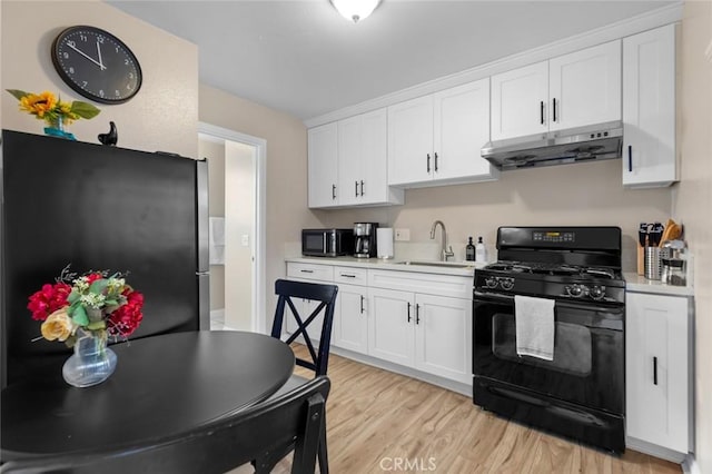 kitchen with light countertops, freestanding refrigerator, white cabinetry, black gas stove, and under cabinet range hood