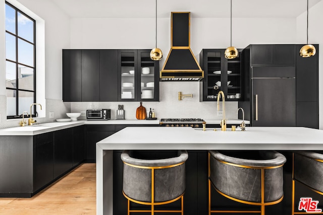 kitchen featuring decorative light fixtures, light hardwood / wood-style floors, custom range hood, and decorative backsplash