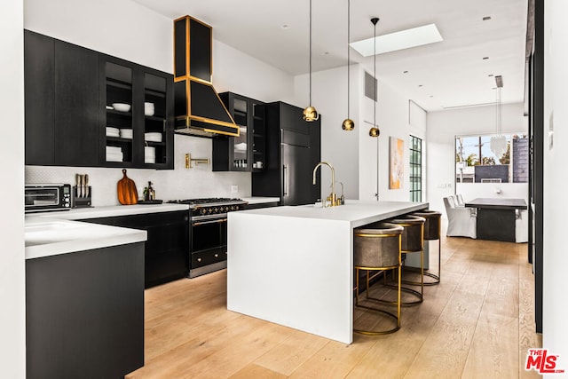 kitchen featuring extractor fan, a kitchen breakfast bar, hanging light fixtures, double oven range, and light hardwood / wood-style flooring