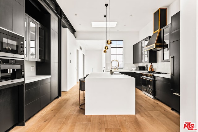 kitchen featuring hanging light fixtures, double oven range, an island with sink, wall oven, and light hardwood / wood-style floors