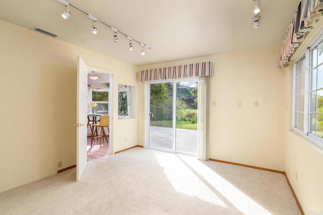 empty room with track lighting, baseboards, visible vents, and light carpet