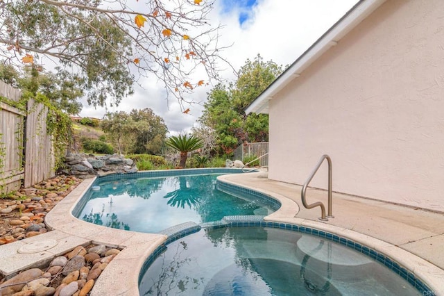 view of pool featuring a patio area, fence, and a pool with connected hot tub