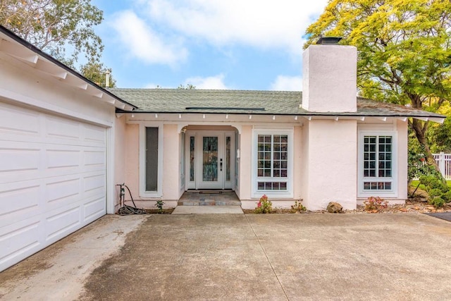 property entrance with a shingled roof, a chimney, a garage, and stucco siding