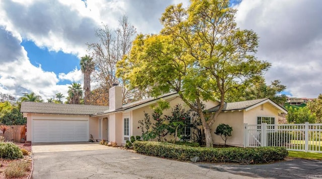 ranch-style house with fence, concrete driveway, stucco siding, a chimney, and an attached garage