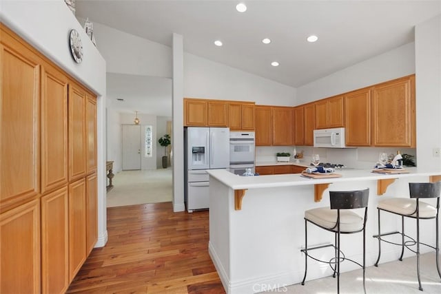 kitchen with white appliances, light countertops, a peninsula, and a kitchen bar