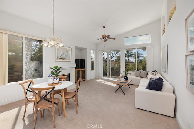 dining area featuring high vaulted ceiling, light colored carpet, ceiling fan with notable chandelier, baseboards, and a glass covered fireplace