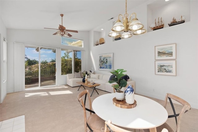 dining area with visible vents, baseboards, light colored carpet, high vaulted ceiling, and ceiling fan with notable chandelier