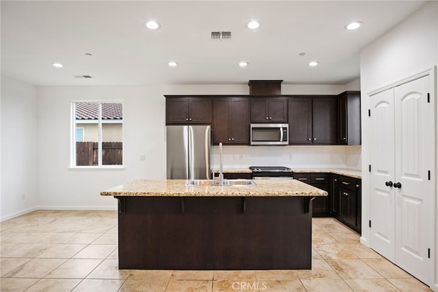 kitchen with appliances with stainless steel finishes, light stone countertops, sink, and a center island with sink