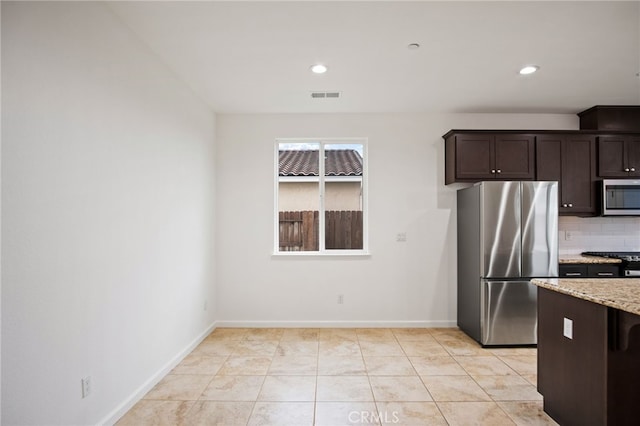 kitchen featuring light tile patterned floors, dark brown cabinets, stainless steel appliances, light stone countertops, and decorative backsplash