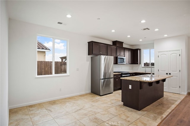 kitchen with sink, a breakfast bar area, stainless steel appliances, light stone counters, and a center island with sink