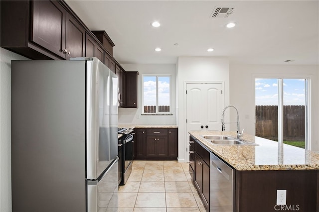 kitchen with an island with sink, sink, backsplash, light stone counters, and stainless steel appliances