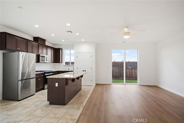 kitchen featuring plenty of natural light, stainless steel appliances, a center island, light stone countertops, and a kitchen bar