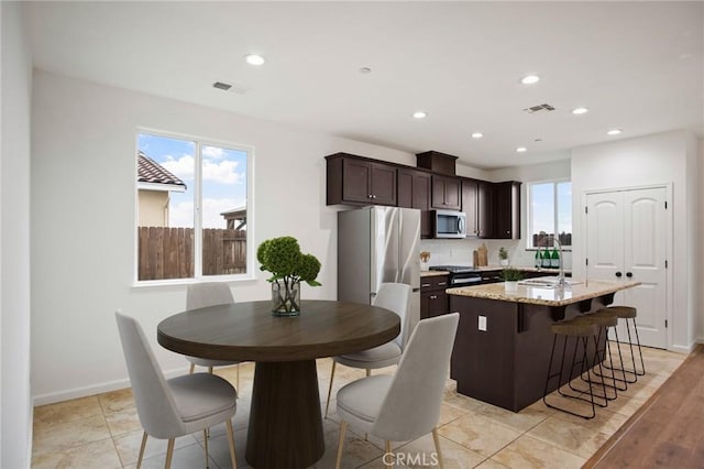 kitchen with appliances with stainless steel finishes, sink, light stone counters, plenty of natural light, and dark brown cabinets