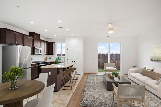 kitchen featuring appliances with stainless steel finishes, a breakfast bar, a center island, light stone countertops, and dark brown cabinets