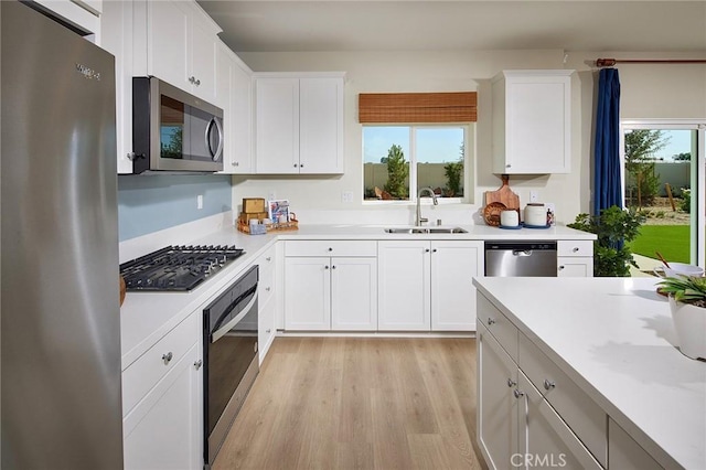 kitchen with appliances with stainless steel finishes, sink, white cabinets, and light wood-type flooring