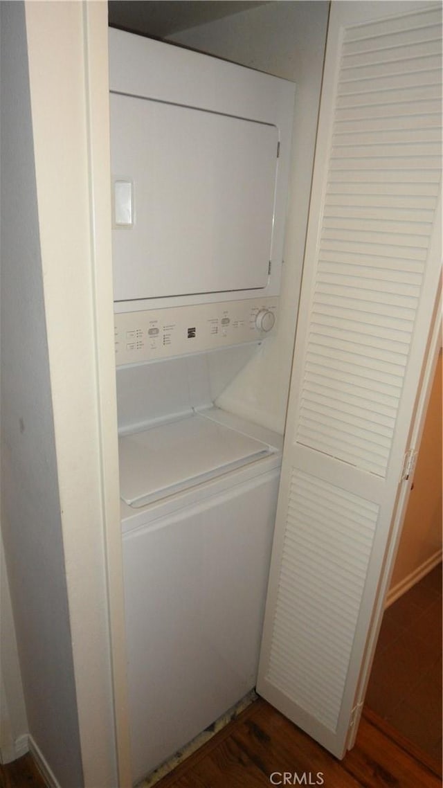 laundry area with dark wood-type flooring and stacked washer / dryer