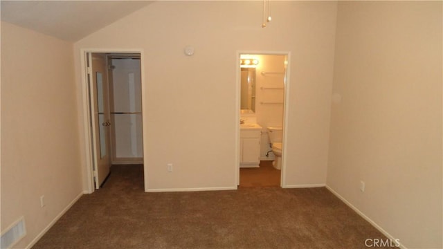 unfurnished bedroom with vaulted ceiling, connected bathroom, sink, dark colored carpet, and a spacious closet