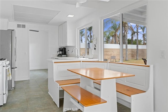 kitchen featuring stainless steel refrigerator, white cabinetry, sink, light tile patterned floors, and gas range gas stove