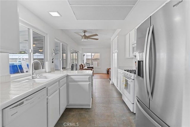 kitchen with sink, white appliances, kitchen peninsula, ceiling fan, and white cabinets