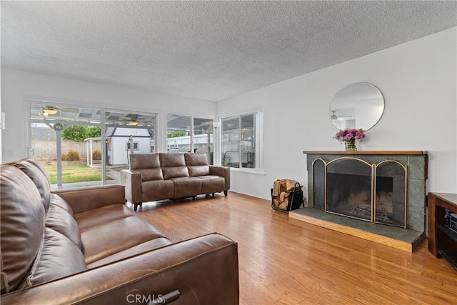 living room with ceiling fan, wood-type flooring, a tile fireplace, and a textured ceiling