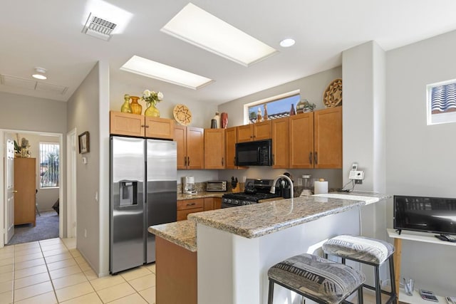 kitchen with a breakfast bar area, light tile patterned floors, appliances with stainless steel finishes, kitchen peninsula, and light stone countertops