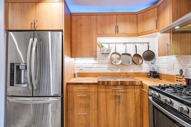 kitchen with wood counters, decorative backsplash, wall chimney exhaust hood, and appliances with stainless steel finishes