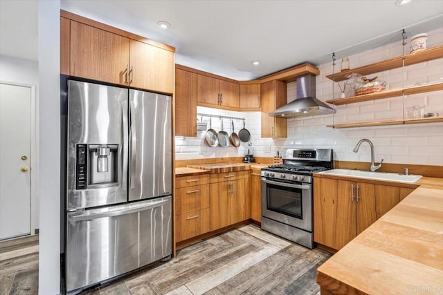 kitchen with appliances with stainless steel finishes, butcher block countertops, sink, backsplash, and wall chimney exhaust hood