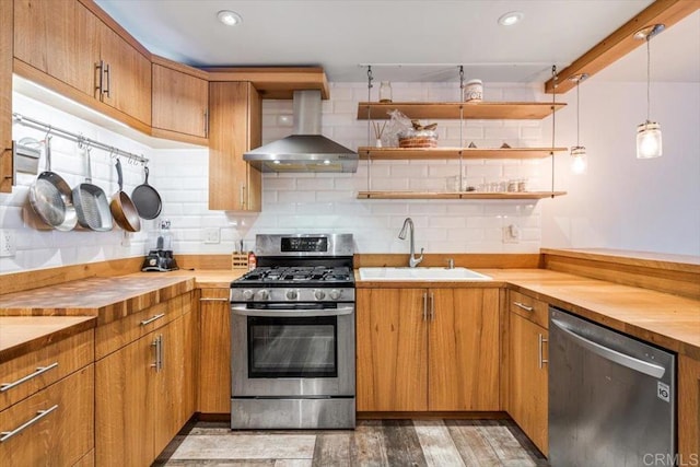 kitchen featuring pendant lighting, wooden counters, wall chimney exhaust hood, and appliances with stainless steel finishes