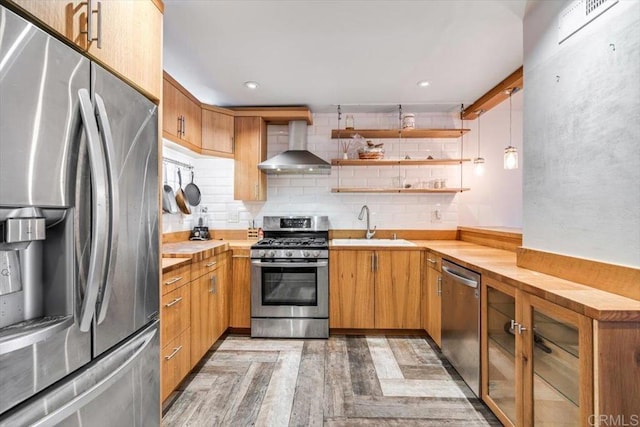 kitchen featuring wall chimney exhaust hood, butcher block counters, sink, hanging light fixtures, and appliances with stainless steel finishes