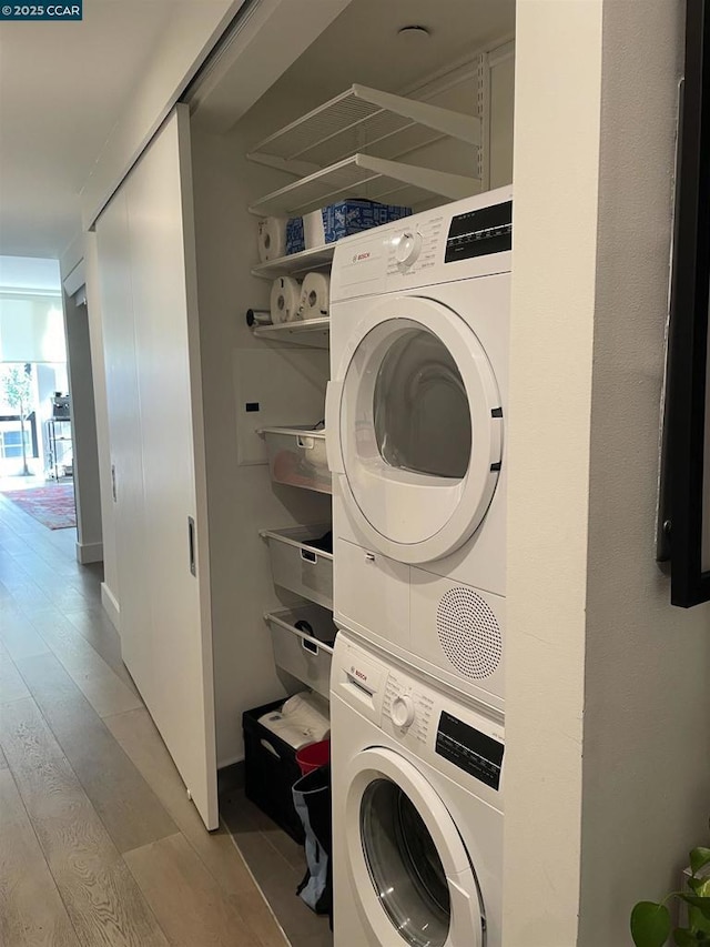 clothes washing area featuring stacked washer and clothes dryer and light hardwood / wood-style floors