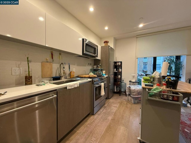 kitchen with sink, stainless steel appliances, white cabinets, and light wood-type flooring