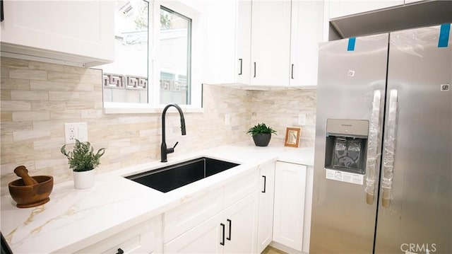 kitchen with white cabinetry, sink, backsplash, light stone counters, and stainless steel fridge with ice dispenser