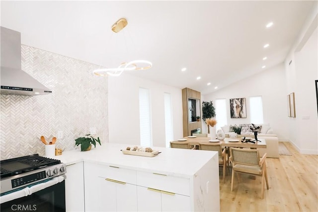 kitchen with wall chimney exhaust hood, white cabinetry, decorative light fixtures, light wood-type flooring, and stainless steel range with gas cooktop