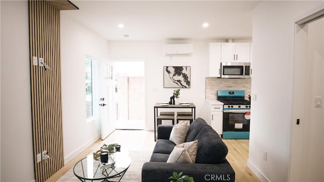 living room featuring an AC wall unit, a healthy amount of sunlight, and light hardwood / wood-style flooring