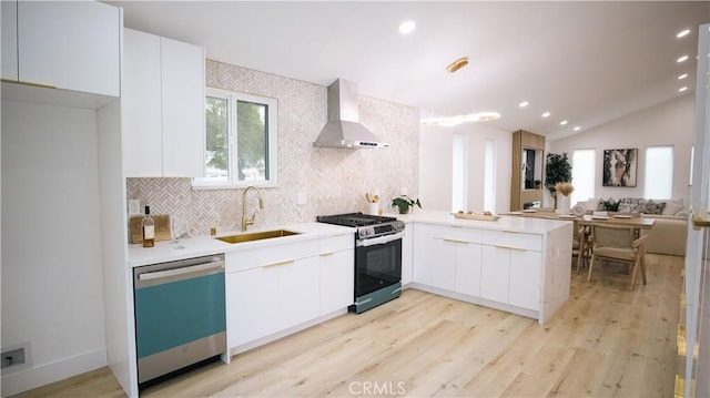 kitchen with sink, white cabinets, kitchen peninsula, stainless steel appliances, and wall chimney exhaust hood